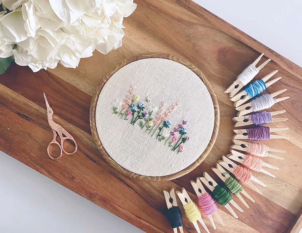 An embroidery hoop and rows of coloured thread on a wooden board