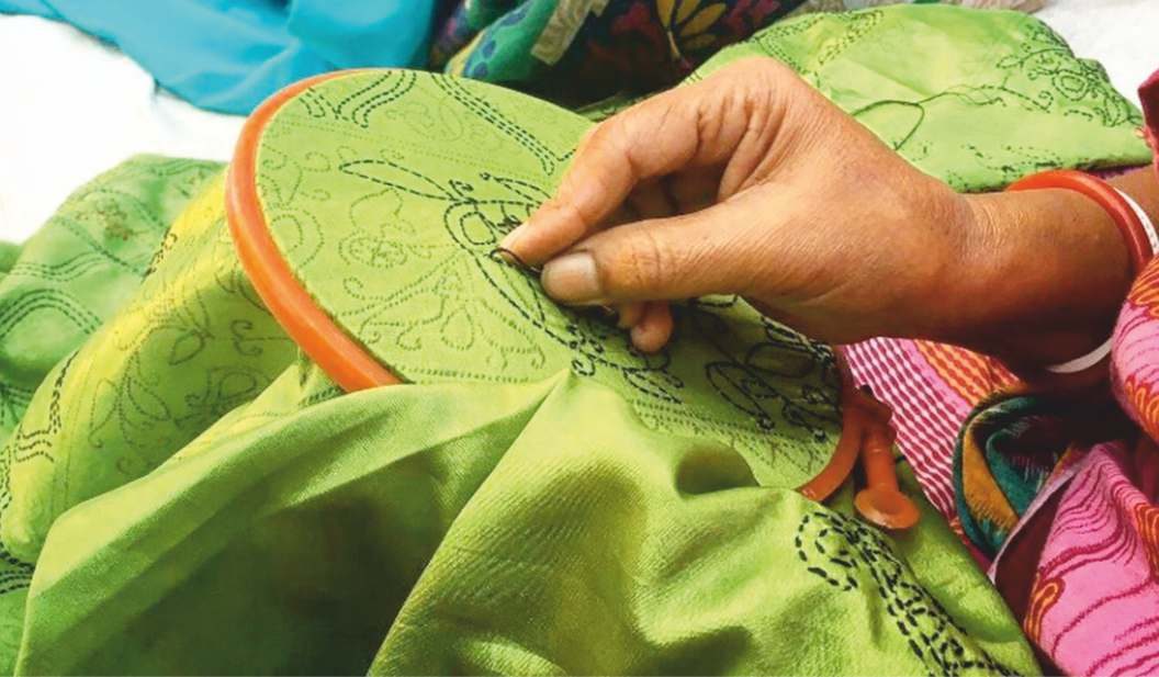 Hands embroidering a green cloth held in a wooden hoop